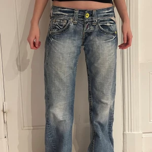 Blå Replay jeans - Säljer ett par blå Replay jeans med coolt slitna detaljer, kontrastsömmar och en broderad gul patch bak. Jeansen är i storlek W27, L32