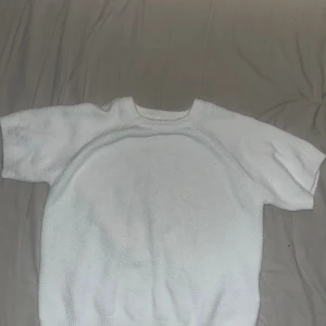 Vit stickad kortärmad tröja - En enkel och stilren vit stickad tröja med korta ärmar och rund hals. Tröjan har ribbade muddar vid hals och nederkant, vilket ger en snygg och clean look. Perfekt för dig som gillar minimalistisk stil och vill ha något mjukt och bekvämt.
