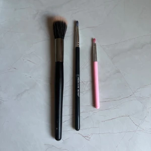 Set med sminkborstar och ögonskuggsborstar - Tre sminkborstar: en stor borste med svart handtag och ljusa borst, en svart ögonskuggsborste från Princess Rose och en liten ögonskuggsborste med rosa handtag. Perfekta för både bas och detaljerad ögonskuggning.