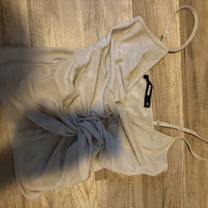 Beige omlott linnetopp från Bik Bok - Säljer en beige linnetopp från Bik Bok i storlek XS. Toppen har tunna justerbara axelband, omlott-detalj framtill och ett snyggt knyt som ger en cool look. Materialet är ribbat och toppen är croppad, perfekt för att styla med höga jeans.