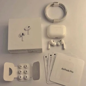 AirPods Pro - Apple AirPods Pro med laddningsetui, extra öronkuddar, laddningskabel och originalförpackning. Produkten seri ut att vara i mycket gott skick utan synligt slitage. Aktiv brusreducering och trådlös anslutning för bästa ljudupplevelse. Komplett med manualer och tillbehör.