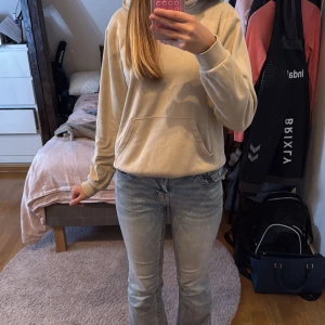 Beige hoodie med huva och ficka - En stilren beige hoodie med huva och stor magficka. Tröjan har långa ärmar och en relaxed passform. Perfekt för chill dagar och enkel att matcha med jeans eller mjukisbyxor.