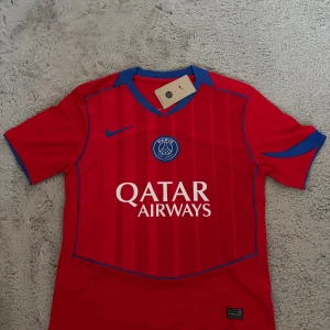 PSG röd matchtröja Nike - Paris Saint-Germain fotbollströja i rött med blå detaljer och diskreta ränder. Tröjan har klubbmärke och Nike-logga på bröstet samt Qatar Airways-tryck. Tillverkad i lätt och ventilerande material, perfekt för träning eller match.