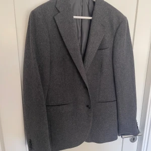 Grå kavaj från These Glory Days - Snygg grå kavaj från These Glory Days i klassisk modell. Tillverkad i 100% ull med foder av polyester och viskos. Perfekt för dig som gillar stilrena och tidlösa plagg.