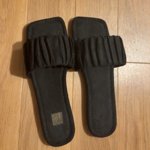Svarta sandaler - Svarta sandaler med bred, rynkad rem över foten och fyrkantig tå. Platt sula och öppen design.