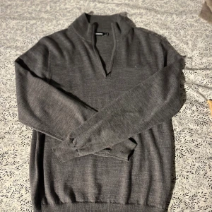 Grå half zip-tröja från J.Lindeberg - Snygg grå stickad tröja från J.Lindeberg med half zip och hög krage. Tröjan har lång ärm och diskret logga på bröstet. Perfekt för lager-på-lager och passar till både jeans och chinos.