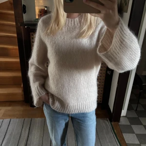 Beige stickad tröja med breda ärmar - Mysig och fluffig beige stickad tröja med breda, långa ärmar och ribbade muddar. Tröjan har en rund halsringning och är perfekt för lager-på-lager under kyliga dagar. Enkel och stilren design som passar till jeans eller kjol. I ull så perfekt till vintern! Köpt för 1500kr!