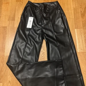 Svarta vida skinnbyxor i XS - Snygga svarta skinnbyxor från Designby Si. Vida ben och klassisk midja, tillverkade i Italien. Materialet är 100% polyuretan på utsidan och 100% polyester på insidan. Perfekta för dig som vill ha en edgy och trendig look.