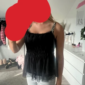 Svart linnetopp med volangdetalj - Säljer en svart linnetopp med smockad midja och volang nertill. Toppen är ärmlös och har en luftig känsla, perfekt för varma dagar.