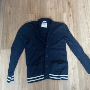 Mörkblå kofta Abercrombie & Fitch  - Snygg mörkblå kofta från Abercrombie & Fitch i storlek M. Koftan har knappar framtill, två fickor och vita ränder vid ärmslut och nederkant. Perfekt för lager-på-lager och chill stil.