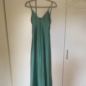 Grön långklänning från Zara - Snygg grön långklänning från Zara med tunna axelband och v-ringning. Klänningen har en elegant, slät yta och öppen rygg som ger en stilren look. Perfekt för dig som gillar minimalistisk stil och vill sticka ut med en fräsch färg.
