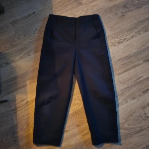 Byxor Cos  - Snygga svarta kostymbyxor med raka ben. Byxorna har diskreta bakfickor och stängs med dragkedja och hyska. Perfekta för en clean och stilren look. Materialet känns mjukt och har en lätt stretch. Storlek 34