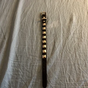 Svart valentino armband  - Säljer ett smalt svart bälte i skinn med coola fyrkantiga silvernitar längs hela bandet. Bältet har ett klassiskt spänne i silverfärg och passar perfekt för att ge din outfit en edgy touch. Funkar både som bälte och armband om du vill ha en alternativ stil.