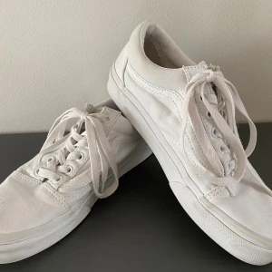 Vita Vans Old Skool sneakers - Klassiska Vans Old Skool sneakers i helvitt canvasmaterial med matchande vita snören och sula. Skorna har den ikoniska sidoranden och låg profil, perfekt för en clean och stilren look. Platt sula och rund tå ger en skön känsla hela dagen. Skorna är endast använda inomhus och är i bra begagnat skick.   Kommer från ett djur och rökfritt hem 