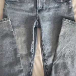 Ljusblå bootcut jeans med knappar - Snygga ljusblå jeans med bootcut passform och klassisk femficksdesign. Jeansen har två bakfickor med lock och silverfärgade knappar framtill. Materialet är slitstarkt jeans och färgen har en lätt tvättad look som ger cool vintagekänsla.