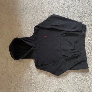 Svart hoodie från Polo Ralph Lauren - Svart hoodie från Polo Ralph Lauren med klassisk röd broderad logga på bröstet. Tröjan har huva, känguruficka och långa ärmar. Tillverkad i mjuk bomull, perfekt för chill dagar eller när du vill ha en clean style.