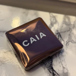 CAIA Bronzer Gold Coast - Snygg bronzer från CAIA i nyansen Gold Coast. Kommer i en lyxig, fyrkantig brun metallic dosa med spegel. Pudret har en varm, gyllene ton och en vågig, pressad yta. Perfekt för att ge ansiktet en solkysst look.