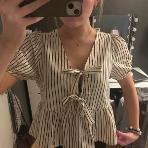 Randig blus från Carin Wester, strl 36 - Säljer en söt blus från Carin Wester i storlek 36. Blusen är vit med svarta vertikala ränder, har puffiga korta ärmar och två knytningar framtill. Den har fått en liten defekt på baksidan (se sista bilden) men verkligen ingenting som man ser eller lägger märker till när man har den på sig. Köpt för 600kr😇😇