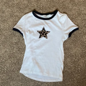 Vit t-shirt med leopardstjärna H&M - Snygg vit t-shirt från H&M med svarta detaljer vid hals och ärmslut. Har inga synliga defekter. 