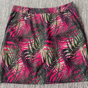 Färgglad skorts, kjol med shorts från Röhnisch - Säljer en skorts, kjol med shorts från Röhnisch med tropiskt bladmönster i rosa, grönt och svart. Kjolen har praktiska fickor, bälteshällor och innerbyxa. Perfekt för dig som gillar färg och vill sticka ut med en cool look. Materialet är lätt och känns bekvämt mot huden. Nya skorts, kjol med shorts i cerise och grönt mönster i strl 40 från Röhnisch.   Nya, aldrig använda   Mått  Midjan: ca 42 cm  Total längd: ca 49 cm   Polyester och elastan   Kommer från ett djur och rökfritt hem. 