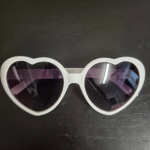 Vita hjärtformade solglasögon - Snygga solglasögon med vit ram och hjärtformade linser. Glasen är mörka och ger en cool kontrast mot den vita plasten. Perfekt för dig som vill sticka ut och addera lite extra attityd till din stil.