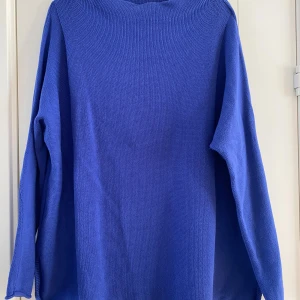 Blå stickad tröja med bred hals - En chill blå stickad tröja med bred halsringning och långärmade ärmar. Modellen är loose fit och har en enkel, stilren design utan mönster eller detaljer. Perfekt för att slänga på sig när det är lite kyligt ute. Mått Över bröstet: ca 62 cm Längd från axeln och ner: ca 71 cm  100% bomull  Kommer från ett djur och rökfritt hem. 