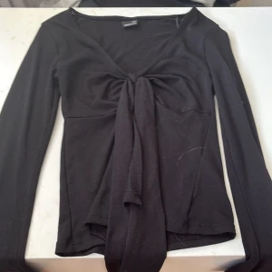 Svart omlottopp från Gina Tricot - Svart långärmad omlottopp från Gina Tricot i mjukt material. Toppen har en snygg v-ringning och knyt framtill som ger en trendig look. Perfekt att styla med jeans eller kjol för en cool outfit. I strl xxs 