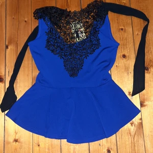 Blå peplum blus med spets från Nikka - Säljer en snygg blå peplum blus från Nikka med svart spetsdetalj i halsen och breda svarta band att knyta i nacken. Blusen är ärmlös och har en feminin siluett med volang nedtill. Materialet är mjuk polyester med lite stretch för skön passform.