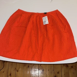 Orange kjol från H&M, storlek 38 - Säljer en snygg orange kjol från H&M i storlek 38. Kjolen har en cool textur med diskret mönster och dragkedja bak. Passformen är normal och tyget känns lätt och bekvämt. Perfekt för dig som vill sticka ut med färg och stil.