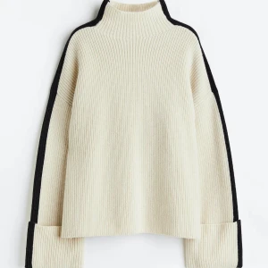 Beige ribbad polotröja med svarta detaljer - Säljer en beige ribbad polotröja från H&M med svarta ränder längs axlar och ärmar. Tröjan har hög krage, lång ärm och loose passform. 