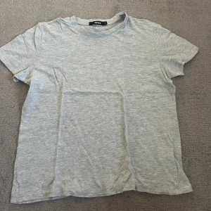 Grå basic t-shirt från Bik Bok - Enkel och stilren grå t-shirt från Bik Bok i storlek M. T-shirten har rund halsringning och korta ärmar, perfekt för en avslappnad look. Tillverkad i mjuk bomull.