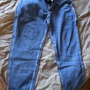 Blå jeansbyxor från Dickies W36/L32 - Säljer ett par klassiska blå jeansbyxor från Dickies med raka ben och stora bakfickor. Byxorna har en loose passform och är tillverkade i slitstarkt bomullsjeans. Perfekta för dig som gillar streetwear och vill ha en avslappnad look.