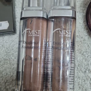 Mist Stockholm Excellence Foundation - Två flytande foundations från Mist Stockholm i genomskinliga pumpflaskor. Ena har en varm beige ton och den andra är något ljusare. Perfekt för att skapa en jämn och naturlig bas. Snygg och stilren förpackning i plast.