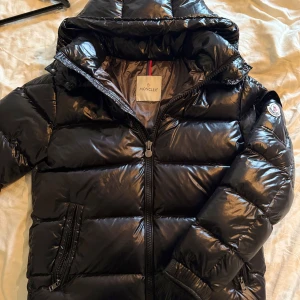MONCLER Maya Puffer jacka, strl 1/S - Snygg svart pufferjacka från Moncler med glansig finish och klassisk logga på ärmen. I nytt, knappt använt skick.  Jackan är i storlek 1, vilket motsvarar storlek S. Passar till både dam och herr! Nypris är 17 999kr, säljes billigt då jag vill köpa en ny vinterjacka. 