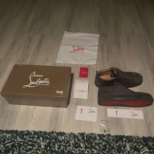 Christian Louboutin - Snygga grå sneakers från Christian Louboutin i mocka med ikoniska röda sulor och coola nitar på tån. Box,påse och 3 nitar följer med. Bra skick alla nitar är kvar,men lite färg har skavts bort. Priset är inte hugget i sten!