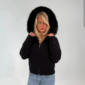 Alessi Jacka  - Snygg svart teddyjacka med fluffig pälsdetalj på huvan och grov ribbad kant vid ärmslut och nederkant. Jackan har dragkedja framtill och en loose passform som ger en chill vibe. Perfekt för kalla dagar när du vill vara både varm och stilren.