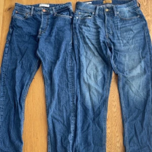 2 par blåa jeans Jack & Jones 28/32 - Två par blå jeans från Jack & Jones, ena modellen Cropped/Frank och andra Loose/Chris. Båda i klassisk blå tvätt, Cropped/Frank har croppad passform och Loose/Chris är loose fit. Snygga detaljer med kontrastsömmar och klassiska fem fickor. Perfekta för en avslappnad stil.