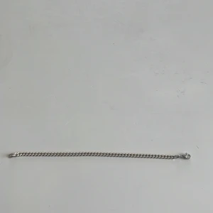 Silver Armband - Snyggt armband i silver med klassisk kedjedesign. Länkarna är platta och blanka, vilket ger en stilren och modern look. Perfekt att bära ensam eller att kombinera med andra smycken för en personlig stil.