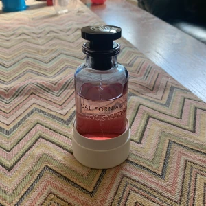 Louis Vuitton California Dream parfym - Lyxig parfym från Louis Vuitton, modellen California Dream. Flaskan är rund och gjord av glas med en snygg rosa ton på vätskan. Svart lock med LV-logga i vitt. Kommer med vit cylinderformad förpackning med präglad logga. Perfekt för dig som gillar exklusiva dofter.