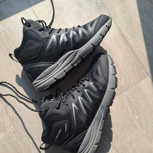 Svarta kängor Sprayway dam strl 39 - Svarta kängor från Sprayway i storlek 39. Skorna är vattentäta och andas, med robust snörning och slitstark sula. Ovandelen är i syntet och mesh med grå detaljer och reflekterande mönster. Perfekta för utomhusaktiviteter och äventyr.