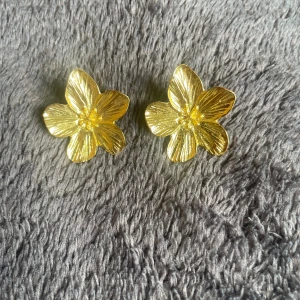 Guldiga blomformade örhängen🤍 - Snygga örhängen i form av blommor med fem blad, helt i guldig färg. De har en tydlig struktur som ger ett lyxigt och trendigt intryck. Perfekta för dig som vill sticka ut med ett statement-smycke🫶🏻
