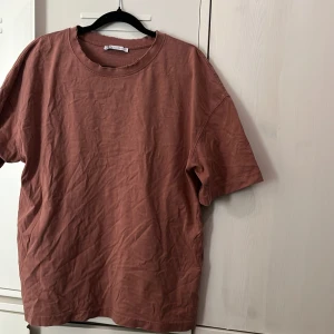 Brun t-shirt från Zara i bomull - En gammelrosa t-shirt från Zara i mjuk bomull med korta ärmar och rå kant vid halsringningen. Oversized fit som ger en chill vibe och passar perfekt till jeans eller shorts. Enkel och stilren design utan tryck eller mönster.