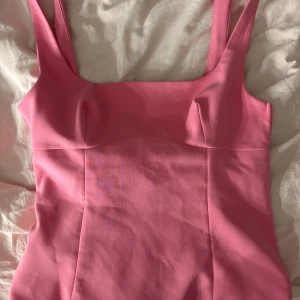 Rosa topp med rosett från Zara - Supersöt rosa topp från Zara med breda axelband och en stor rosett i ryggen. Toppen har figurnära passform och dragkedja i sidan. Är i storlek M och bara använts en gång. På sista bilden ser ni att jag har sytt lite vid dragkedjan då det har låsnat. 