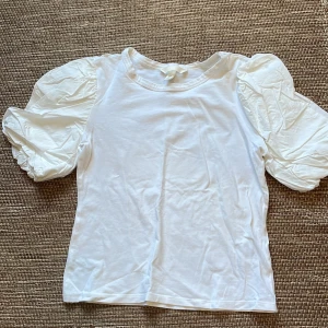 Vit topp med puffärmar - Superfin vit topp från H&M med korta puffärmar och rund halsringning. Toppen är croppad och har en stilren look med voluminösa ärmar som ger en trendig siluett. Perfekt att styla med både jeans och kjol! Skriv till mig vid eventuella frågor eller om du är intresserad💕