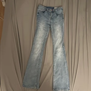 Bootcut jeans från Vero Moda - Snygga ljusblå bootcut jeans från Vero Moda med klassisk femficksdesign och slitna detaljer. Jeansen har normal passform och är tillverkade i mjukt denimtyg med dragkedja och knapp framtill. Perfekt för dig som gillar retrovibbar och avslappnad stil. I storlek S. Jeansen kostade ungefär 600kr.