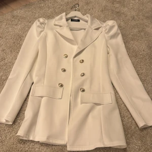 Vit kavaj me guld knappar  - Säljer en ass snygg vit kavaj som sitter jötte fint me guld knappar vid magen och på armen puffiga armar som ger en mer gulligare och coolare still 