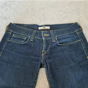 Mörkblå bootcut jeans med låg midja - Midja: 82 innerben: 81. Snygga mörkblå jeans med bootcut och låg midja. Klassisk femficksmodell med kontrastsömmar och dragkedja. Jeansen har en figurnära passform upptill och utsvängda ben, vilket ger en riktigt schysst siluett. Perfekta till sneakers eller boots.