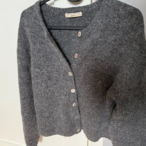 Grå stickad kofta från Gina Tricot - Mysig grå stickad kofta från Gina Tricot i storlek XS. Koftan har en rak passform, långa ärmar och knäppning med ljusa knappar framtill. Perfekt för lager-på-lager och chill dagar.