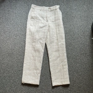 Beiga strukturerade kostymbyxor - Säljer ett par beiga kostymbyxor med snygg struktur och raka ben. Byxorna har hög midja, bälteshällor och sidfickor. Materialet känns lite tjockare och ger en exklusiv känsla. Perfekta för dig som vill ha en clean och stilren look. Dom sitter jätte bra på rumpan! 