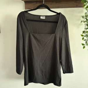 Svart ribbad topp från Noisy May - Svart ribbad topp från Noisy May med fyrkantig ringning och trekvartsärm. Tunn och stretchig. Finns en lös tråd på framsidan. 